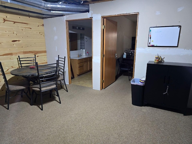 dining space featuring wood walls, sink, and light colored carpet