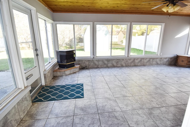 unfurnished sunroom featuring a wood stove, ceiling fan, and wooden ceiling