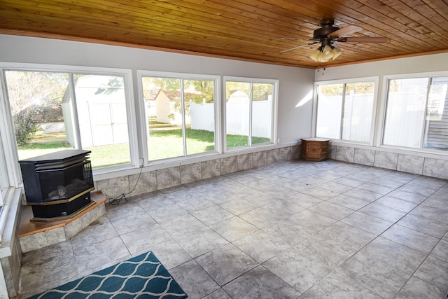 unfurnished sunroom featuring ceiling fan, a wood stove, and wood ceiling