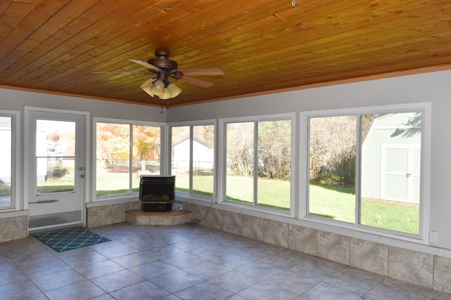 unfurnished sunroom with ceiling fan, a wood stove, a wealth of natural light, and wood ceiling