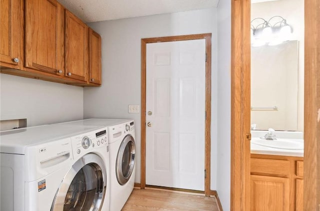 laundry area featuring cabinets, a textured ceiling, light hardwood / wood-style flooring, sink, and washer and clothes dryer