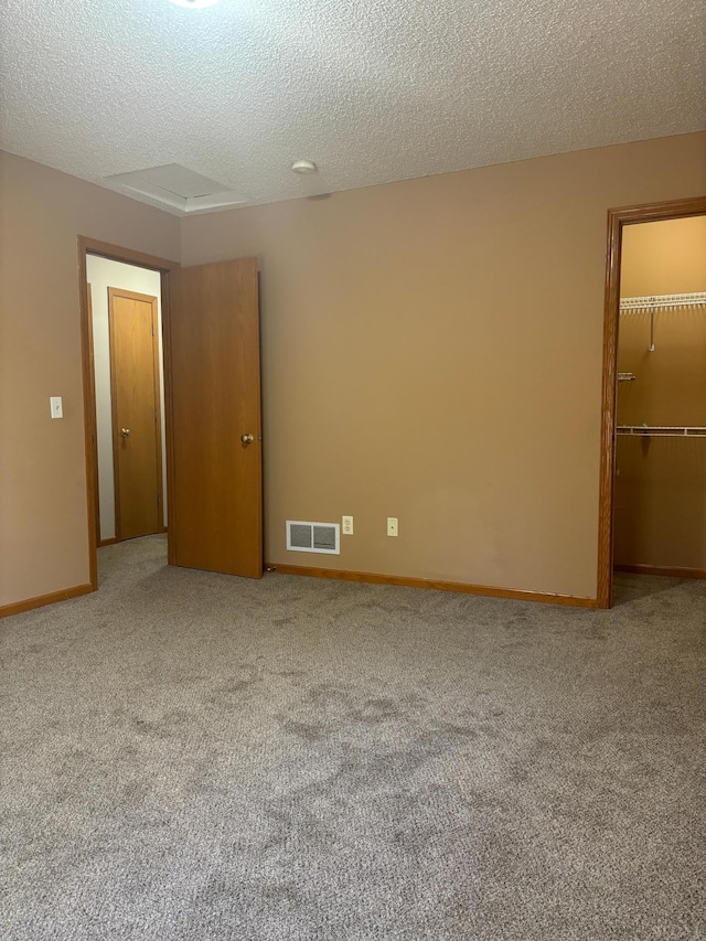 unfurnished bedroom featuring a closet, a textured ceiling, a spacious closet, and light colored carpet