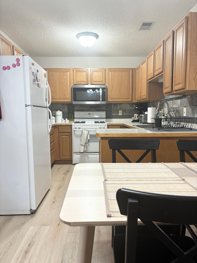 kitchen featuring backsplash, a breakfast bar, light wood-type flooring, a textured ceiling, and white appliances