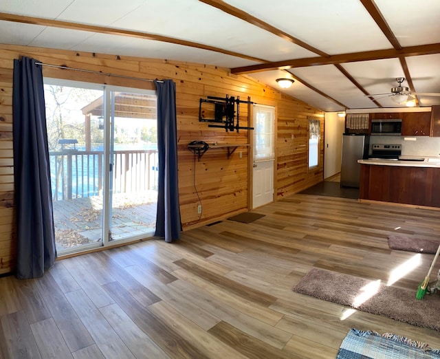 kitchen with kitchen peninsula, stainless steel appliances, lofted ceiling with beams, hardwood / wood-style flooring, and wood walls