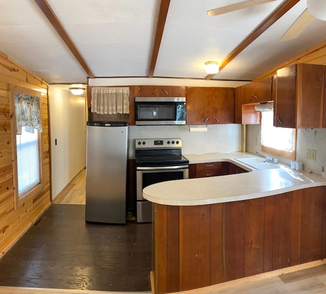 kitchen featuring kitchen peninsula, appliances with stainless steel finishes, light wood-type flooring, sink, and wood walls