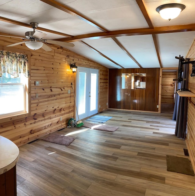 unfurnished living room featuring hardwood / wood-style flooring, plenty of natural light, lofted ceiling with beams, and wooden walls