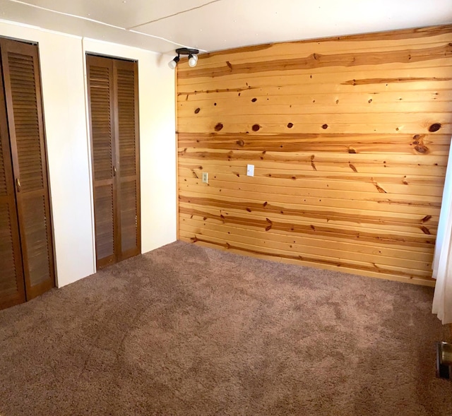 unfurnished bedroom featuring carpet floors, wooden walls, and two closets