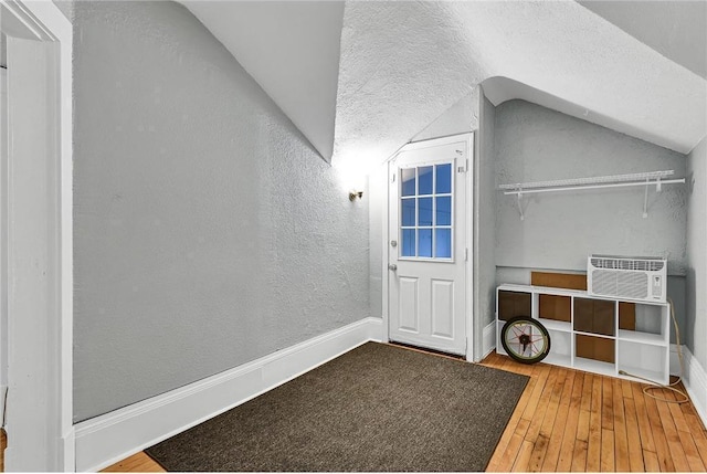 interior space with lofted ceiling, a textured ceiling, a wall unit AC, and wood-type flooring