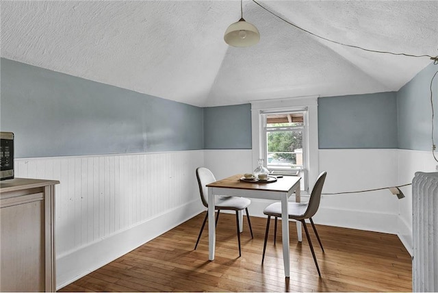 dining area with a textured ceiling, vaulted ceiling, and hardwood / wood-style flooring