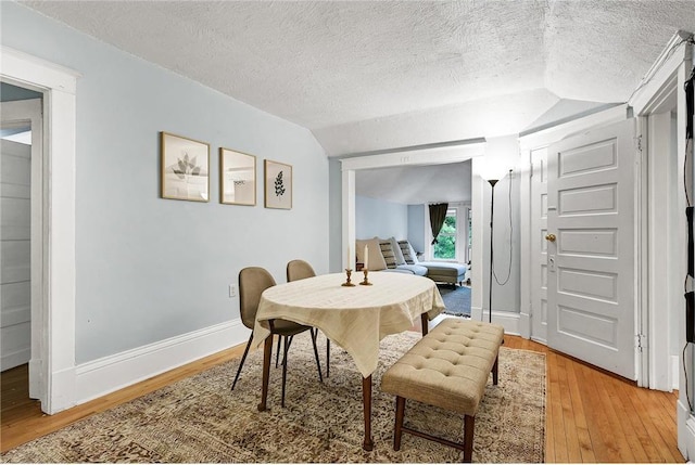 dining space featuring a textured ceiling, vaulted ceiling, and wood-type flooring