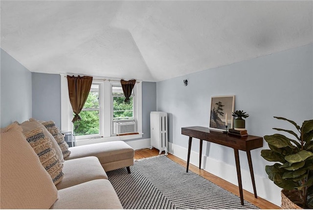 sitting room with lofted ceiling, cooling unit, hardwood / wood-style floors, a textured ceiling, and radiator heating unit