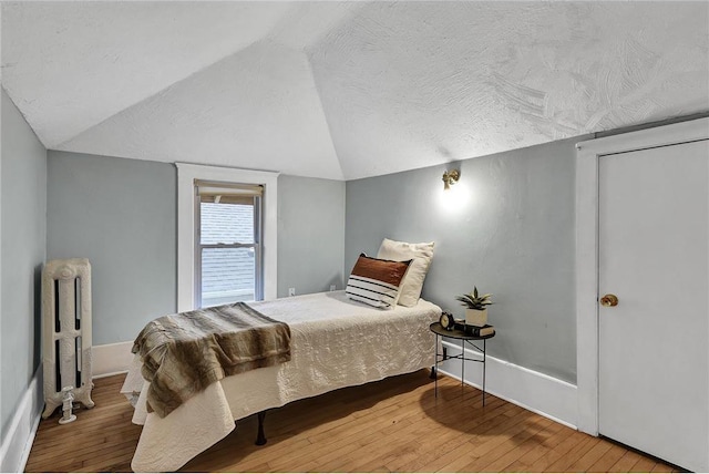 bedroom with lofted ceiling, a textured ceiling, wood-type flooring, and radiator