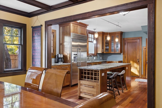 kitchen with stainless steel built in fridge, hardwood / wood-style floors, hanging light fixtures, sink, and a center island