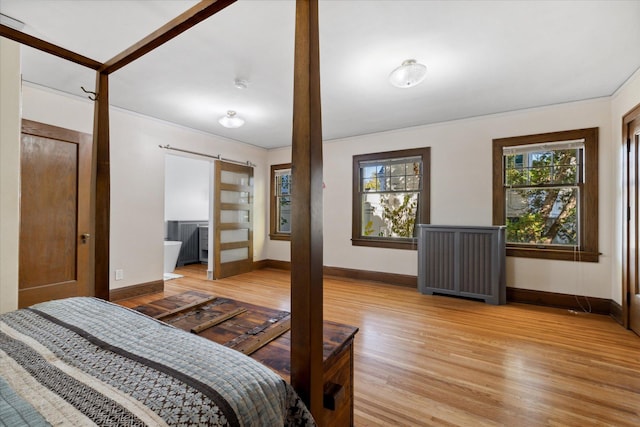 bedroom featuring radiator heating unit, light hardwood / wood-style floors, ensuite bathroom, and a barn door