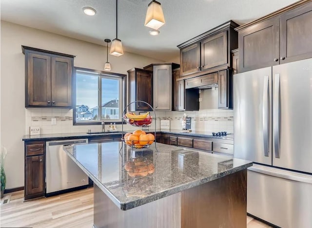 kitchen featuring tasteful backsplash, dark stone countertops, stainless steel appliances, decorative light fixtures, and a center island