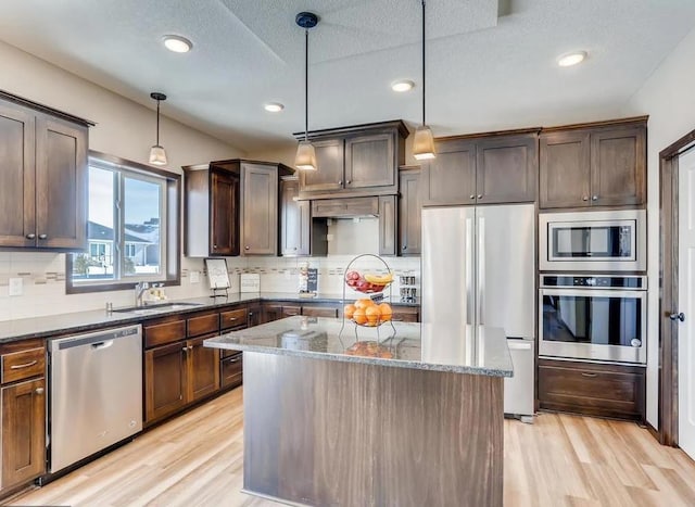 kitchen with hanging light fixtures, dark stone countertops, stainless steel appliances, sink, and a center island