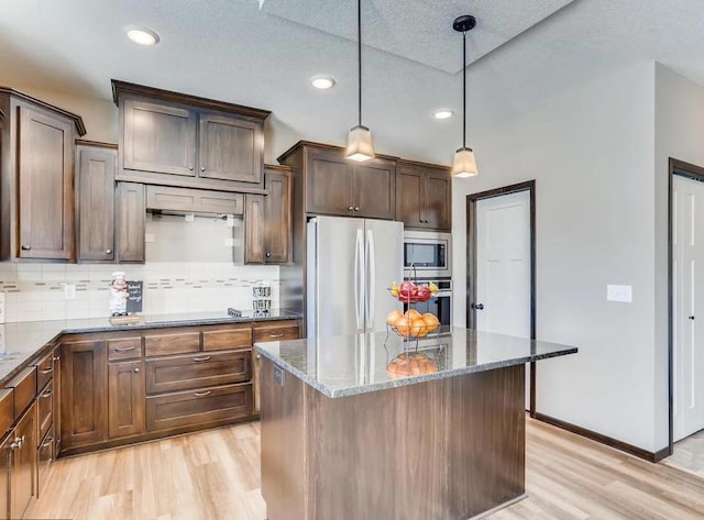 kitchen with light hardwood / wood-style floors, appliances with stainless steel finishes, dark stone counters, and a kitchen island