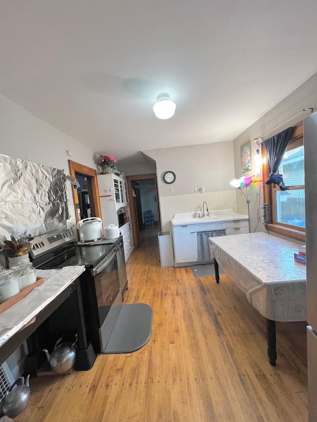 kitchen with washer / dryer, light hardwood / wood-style flooring, white cabinetry, and stainless steel range with electric cooktop