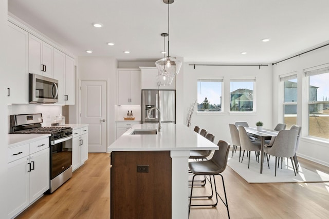 kitchen with a center island with sink, appliances with stainless steel finishes, light countertops, and a sink