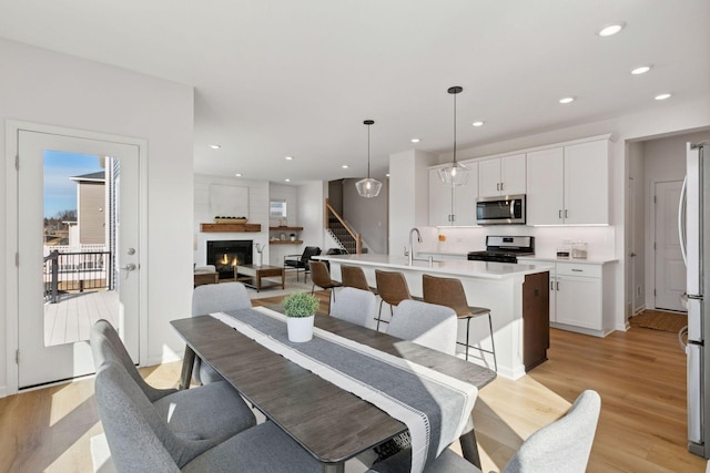 dining room with a warm lit fireplace, recessed lighting, stairs, and light wood-style floors