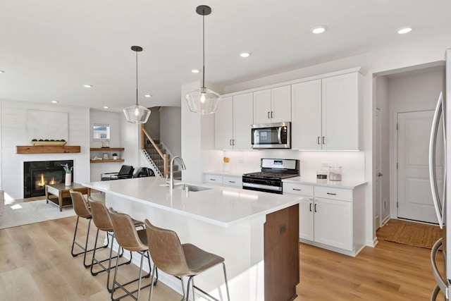 kitchen with stainless steel appliances, a fireplace, a sink, and light wood finished floors