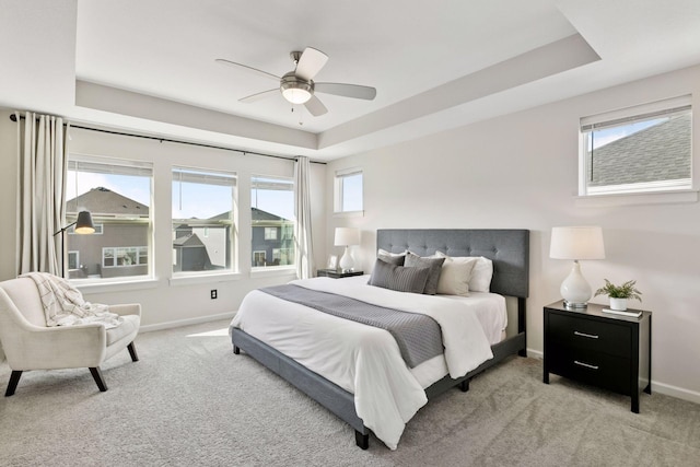 carpeted bedroom featuring baseboards, a raised ceiling, and a ceiling fan