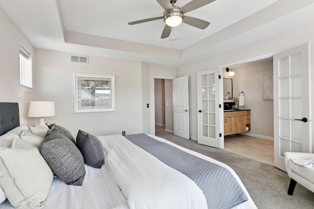 carpeted bedroom with french doors, a raised ceiling, visible vents, connected bathroom, and baseboards