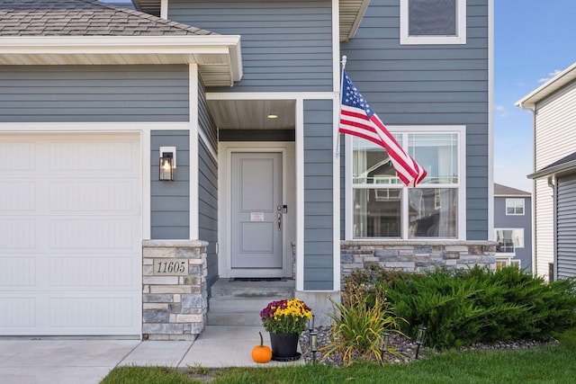 entrance to property with a shingled roof, stone siding, and an attached garage