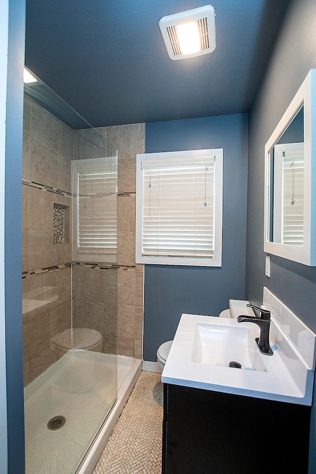 bathroom featuring tile patterned floors, vanity, toilet, and tiled shower