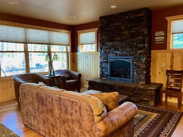 living room with a stone fireplace, hardwood / wood-style floors, and wooden walls