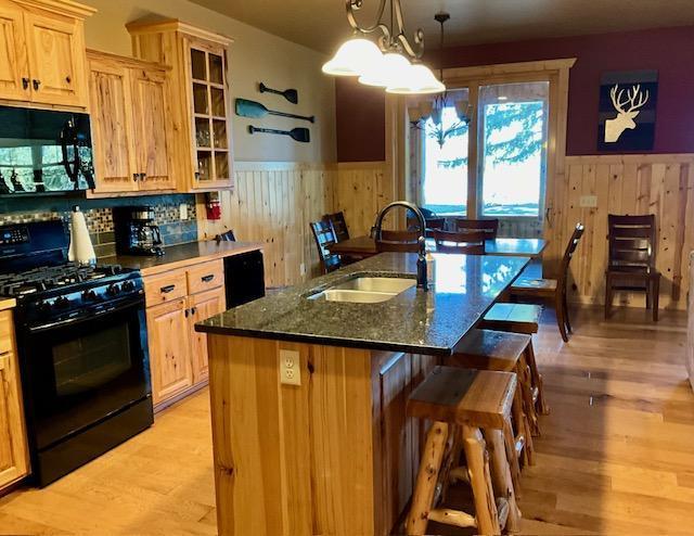 kitchen featuring an island with sink, light hardwood / wood-style flooring, dark stone countertops, black appliances, and sink