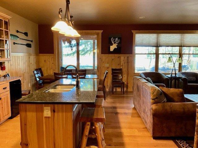 kitchen featuring sink, a kitchen bar, an island with sink, light hardwood / wood-style floors, and dark stone countertops