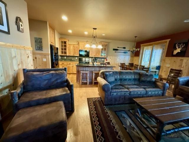 living area featuring a wainscoted wall, light wood-type flooring, a chandelier, and wood walls