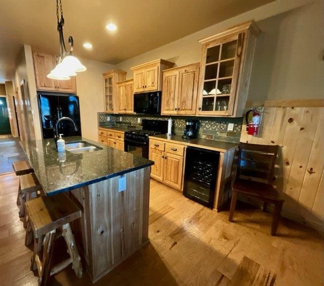 kitchen with wine cooler, hanging light fixtures, light hardwood / wood-style flooring, black appliances, and sink