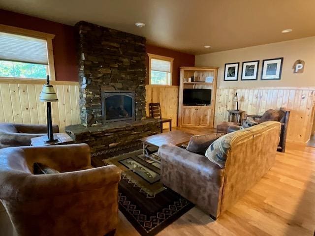 living area with wood walls, wood finished floors, wainscoting, and a stone fireplace