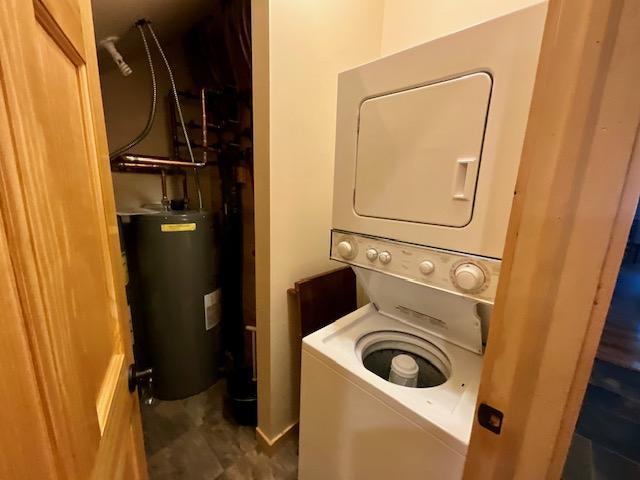 washroom with water heater, stacked washer / dryer, and laundry area