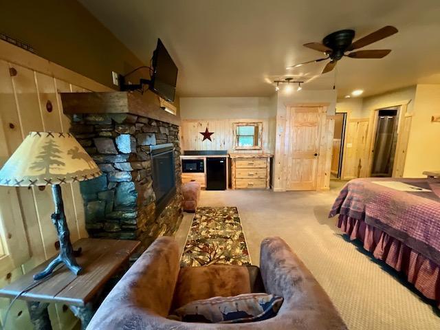 bedroom featuring a stone fireplace, carpet floors, and ceiling fan