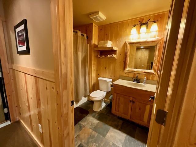 bathroom featuring walk in shower, vanity, toilet, and wood walls