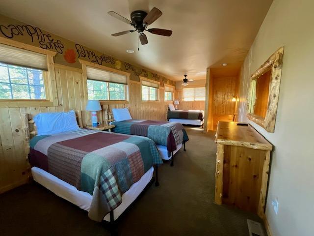 carpeted bedroom featuring wooden walls, multiple windows, and ceiling fan