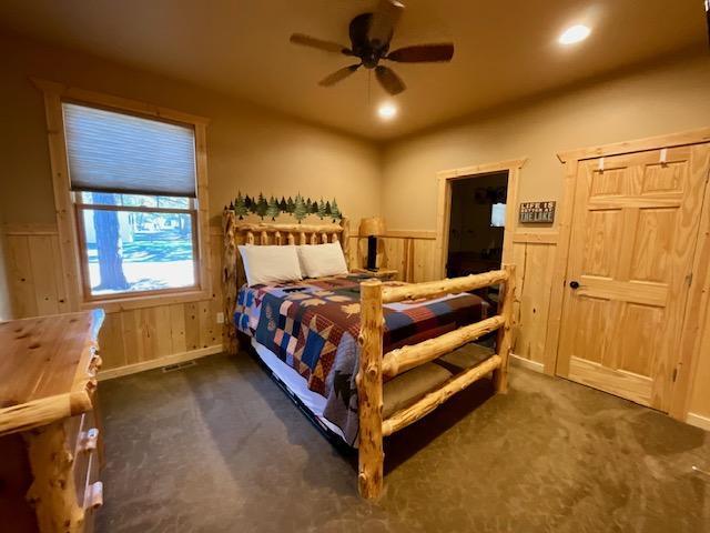 bedroom with dark carpet, wooden walls, and ceiling fan