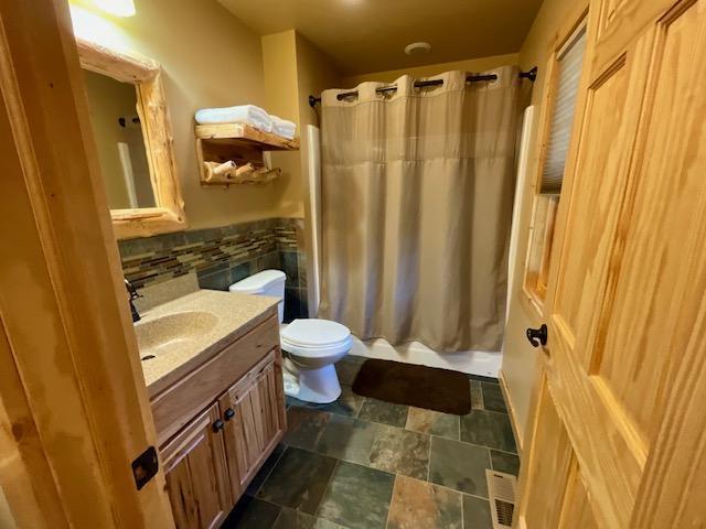 full bathroom featuring shower / tub combo, stone finish floor, toilet, visible vents, and vanity