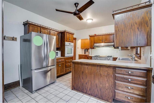 kitchen with sink, kitchen peninsula, ceiling fan, stainless steel appliances, and light tile patterned floors