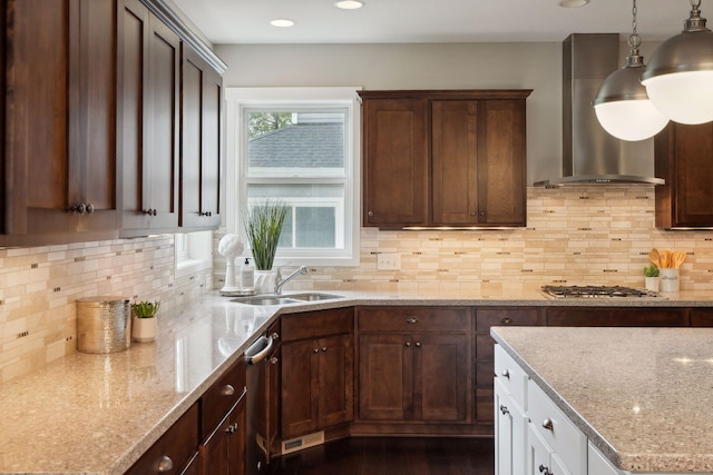 kitchen featuring light stone counters, appliances with stainless steel finishes, pendant lighting, wall chimney exhaust hood, and sink