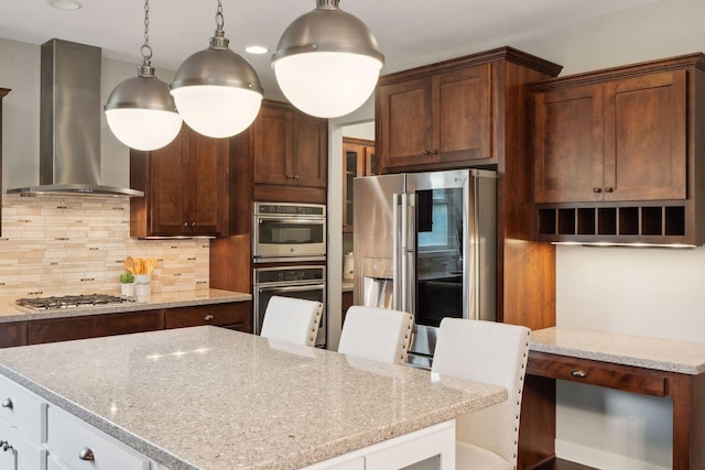 kitchen with wall chimney exhaust hood, a kitchen island, light stone countertops, and stainless steel appliances