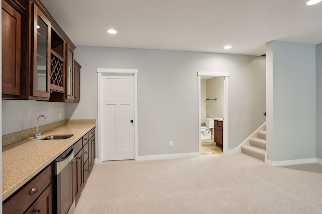 kitchen with light stone countertops, sink, dark brown cabinets, light carpet, and stainless steel dishwasher