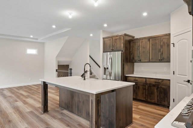 kitchen with a kitchen island with sink, light hardwood / wood-style flooring, stainless steel refrigerator with ice dispenser, sink, and dark brown cabinetry