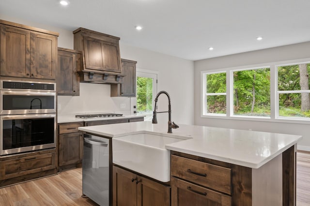 kitchen with a kitchen island with sink, sink, light hardwood / wood-style floors, dark brown cabinetry, and stainless steel appliances