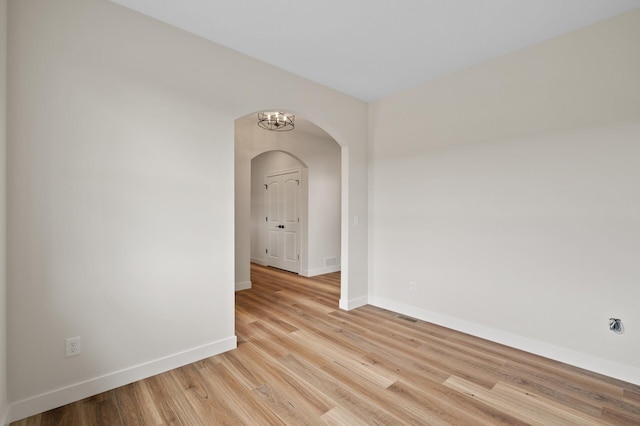 unfurnished room featuring a notable chandelier and light wood-type flooring