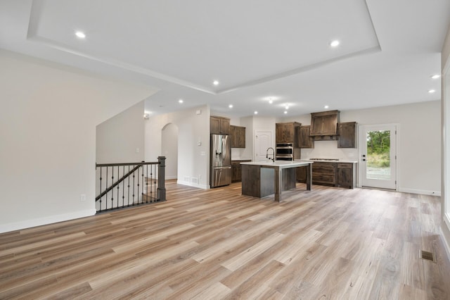 kitchen featuring custom range hood, stainless steel appliances, light wood-type flooring, and a kitchen island with sink