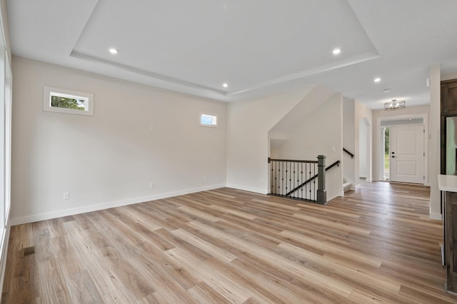 empty room with a notable chandelier, a raised ceiling, and light wood-type flooring